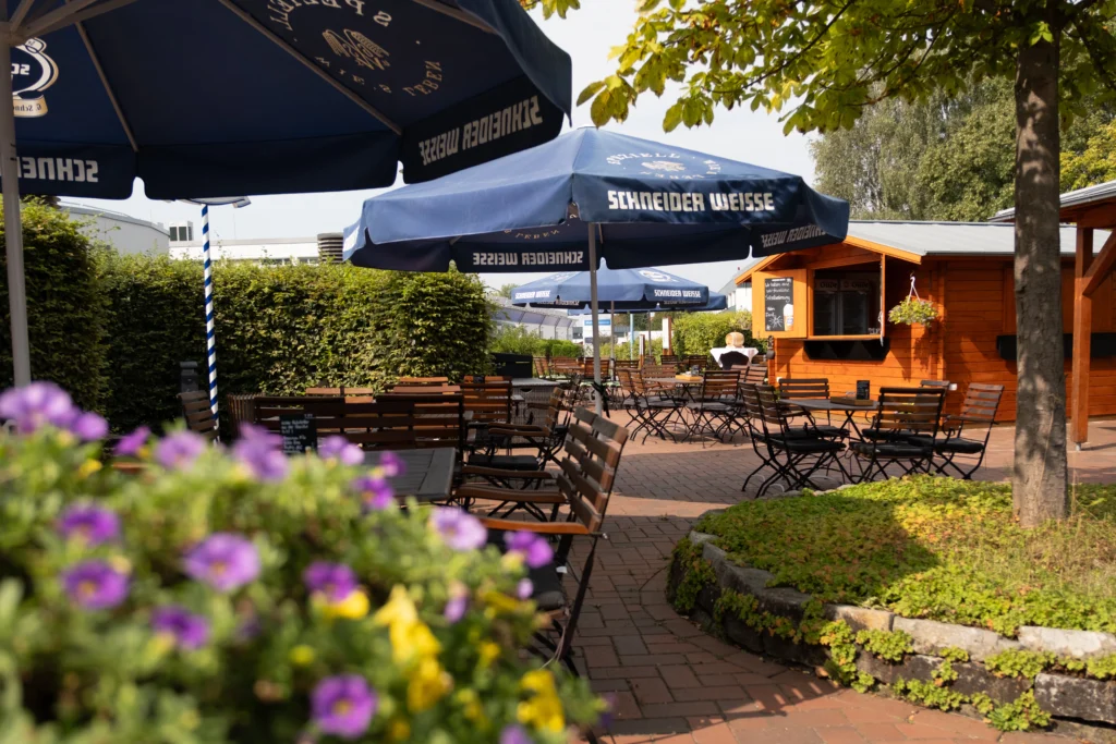 Sonniger Biergarten mit blauen Sonnenschirmen und Holzmöbeln